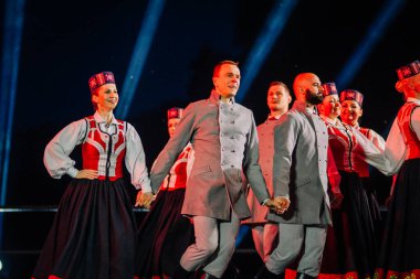 Valmiera, Letonya - 7 Haziran 2025 - GAUJA 80 'deki geleneksel Letonya halk dansları kolajı, renkli kostümlü dansçıları gece aydınlatmalı bir sahnede sergiliyorlar..