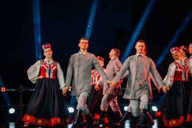 Valmiera, Letonya - 7 Haziran 2025 - GAUJA 80 'deki geleneksel Letonya halk dansları kolajı, renkli kostümlü dansçıları gece aydınlatmalı bir sahnede sergiliyorlar..