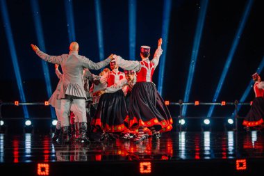 Valmiera, Letonya - 7 Haziran 2025 - GAUJA 80 'deki geleneksel Letonya halk dansları kolajı, renkli kostümlü dansçıları gece aydınlatmalı bir sahnede sergiliyorlar..