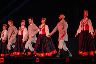 Valmiera, Letonya - 7 Haziran 2025 - GAUJA 80 'deki geleneksel Letonya halk dansları kolajı, renkli kostümlü dansçıları gece aydınlatmalı bir sahnede sergiliyorlar..