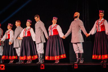 Valmiera, Letonya - 7 Haziran 2025 - GAUJA 80 'deki geleneksel Letonya halk dansları kolajı, renkli kostümlü dansçıları gece aydınlatmalı bir sahnede sergiliyorlar..