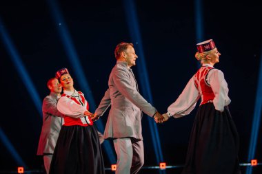Valmiera, Letonya - 7 Haziran 2025 - GAUJA 80 'deki geleneksel Letonya halk dansları kolajı, renkli kostümlü dansçıları gece aydınlatmalı bir sahnede sergiliyorlar..