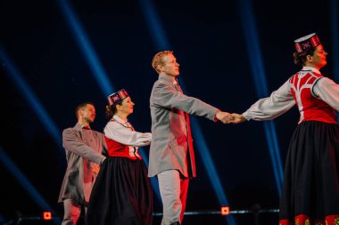 Valmiera, Letonya - 7 Haziran 2025 - GAUJA 80 'deki geleneksel Letonya halk dansları kolajı, renkli kostümlü dansçıları gece aydınlatmalı bir sahnede sergiliyorlar..