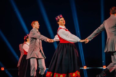 Valmiera, Letonya - 7 Haziran 2025 - GAUJA 80 'deki geleneksel Letonya halk dansları kolajı, renkli kostümlü dansçıları gece aydınlatmalı bir sahnede sergiliyorlar..