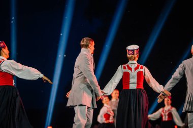 Valmiera, Letonya - 7 Haziran 2025 - GAUJA 80 'deki geleneksel Letonya halk dansları kolajı, renkli kostümlü dansçıları gece aydınlatmalı bir sahnede sergiliyorlar..