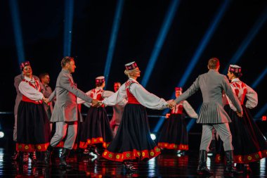 Valmiera, Letonya - 7 Haziran 2025 - GAUJA 80 'deki geleneksel Letonya halk dansları kolajı, renkli kostümlü dansçıları gece aydınlatmalı bir sahnede sergiliyorlar..