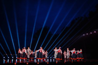 Valmiera, Letonya - 7 Haziran 2025 - GAUJA 80 'deki geleneksel Letonya halk dansları kolajı, renkli kostümlü dansçıları gece aydınlatmalı bir sahnede sergiliyorlar..