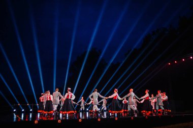 Valmiera, Letonya - 7 Haziran 2025 - GAUJA 80 'deki geleneksel Letonya halk dansları kolajı, renkli kostümlü dansçıları gece aydınlatmalı bir sahnede sergiliyorlar..