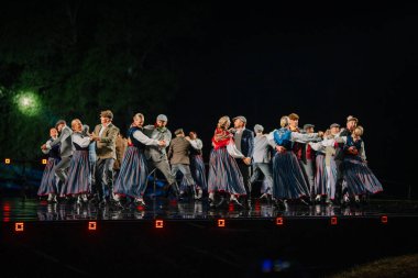 Valmiera, Letonya - 7 Haziran 2025 - GAUJA 80 'deki geleneksel Letonya halk dansları kolajı, renkli kostümlü dansçıları gece aydınlatmalı bir sahnede sergiliyorlar..