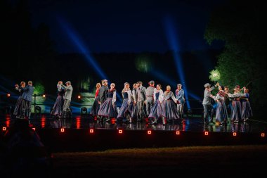 Valmiera, Letonya - 7 Haziran 2025 - GAUJA 80 'deki geleneksel Letonya halk dansları kolajı, renkli kostümlü dansçıları gece aydınlatmalı bir sahnede sergiliyorlar..