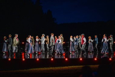 Valmiera, Letonya - 7 Haziran 2025 - GAUJA 80 'deki geleneksel Letonya halk dansları kolajı, renkli kostümlü dansçıları gece aydınlatmalı bir sahnede sergiliyorlar..