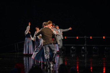 Valmiera, Letonya - 7 Haziran 2025 - GAUJA 80 'deki geleneksel Letonya halk dansları kolajı, renkli kostümlü dansçıları gece aydınlatmalı bir sahnede sergiliyorlar..