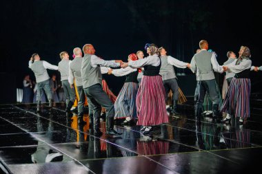 Valmiera, Letonya - 7 Haziran 2025 - GAUJA 80 'deki geleneksel Letonya halk dansları kolajı, renkli kostümlü dansçıları gece aydınlatmalı bir sahnede sergiliyorlar..