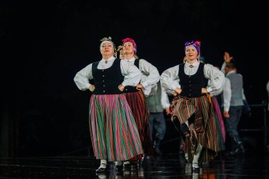 Valmiera, Letonya - 7 Haziran 2025 - GAUJA 80 'deki geleneksel Letonya halk dansları kolajı, renkli kostümlü dansçıları gece aydınlatmalı bir sahnede sergiliyorlar..