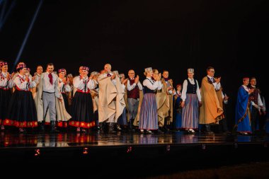 Valmiera, Letonya - 7 Haziran 2025 - GAUJA 80 'deki geleneksel Letonya halk dansları kolajı, renkli kostümlü dansçıları gece aydınlatmalı bir sahnede sergiliyorlar..