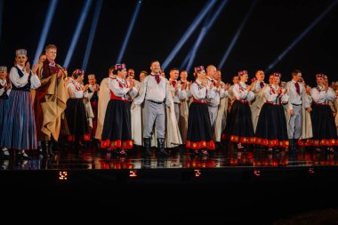 Valmiera, Letonya - 7 Haziran 2025 - GAUJA 80 'deki geleneksel Letonya halk dansları kolajı, renkli kostümlü dansçıları gece aydınlatmalı bir sahnede sergiliyorlar..