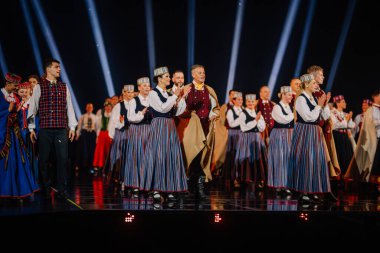Valmiera, Letonya - 7 Haziran 2025 - GAUJA 80 'deki geleneksel Letonya halk dansları kolajı, renkli kostümlü dansçıları gece aydınlatmalı bir sahnede sergiliyorlar..