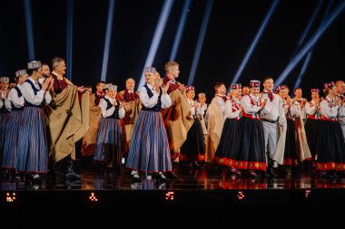 Valmiera, Letonya - 7 Haziran 2025 - GAUJA 80 'deki geleneksel Letonya halk dansları kolajı, renkli kostümlü dansçıları gece aydınlatmalı bir sahnede sergiliyorlar..