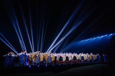 Valmiera, Letonya - 7 Haziran 2025 - GAUJA 80 'deki geleneksel Letonya halk dansları kolajı, renkli kostümlü dansçıları gece aydınlatmalı bir sahnede sergiliyorlar..