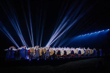 Valmiera, Letonya - 7 Haziran 2025 - GAUJA 80 'deki geleneksel Letonya halk dansları kolajı, renkli kostümlü dansçıları gece aydınlatmalı bir sahnede sergiliyorlar..