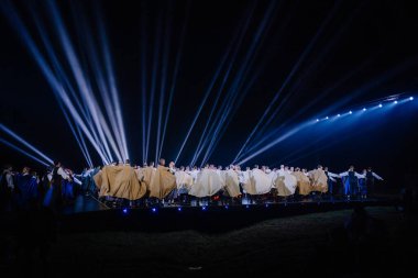 Valmiera, Letonya - 7 Haziran 2025 - GAUJA 80 'deki geleneksel Letonya halk dansları kolajı, renkli kostümlü dansçıları gece aydınlatmalı bir sahnede sergiliyorlar..