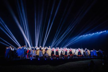 Valmiera, Letonya - 7 Haziran 2025 - GAUJA 80 'deki geleneksel Letonya halk dansları kolajı, renkli kostümlü dansçıları gece aydınlatmalı bir sahnede sergiliyorlar..