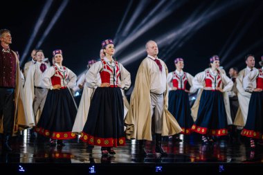 Valmiera, Letonya - 7 Haziran 2025 - GAUJA 80 'deki geleneksel Letonya halk dansları kolajı, renkli kostümlü dansçıları gece aydınlatmalı bir sahnede sergiliyorlar..
