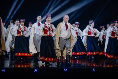 Valmiera, Letonya - 7 Haziran 2025 - GAUJA 80 'deki geleneksel Letonya halk dansları kolajı, renkli kostümlü dansçıları gece aydınlatmalı bir sahnede sergiliyorlar..