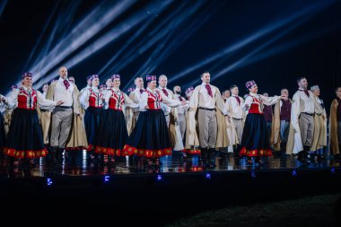Valmiera, Letonya - 7 Haziran 2025 - GAUJA 80 'deki geleneksel Letonya halk dansları kolajı, renkli kostümlü dansçıları gece aydınlatmalı bir sahnede sergiliyorlar..