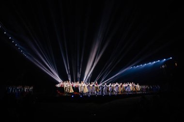 Valmiera, Letonya - 7 Haziran 2025 - GAUJA 80 'deki geleneksel Letonya halk dansları kolajı, renkli kostümlü dansçıları gece aydınlatmalı bir sahnede sergiliyorlar..