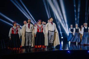Valmiera, Letonya - 7 Haziran 2025 - GAUJA 80 'deki geleneksel Letonya halk dansları kolajı, renkli kostümlü dansçıları gece aydınlatmalı bir sahnede sergiliyorlar..
