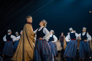 Valmiera, Letonya - 7 Haziran 2025 - GAUJA 80 'deki geleneksel Letonya halk dansları kolajı, renkli kostümlü dansçıları gece aydınlatmalı bir sahnede sergiliyorlar..