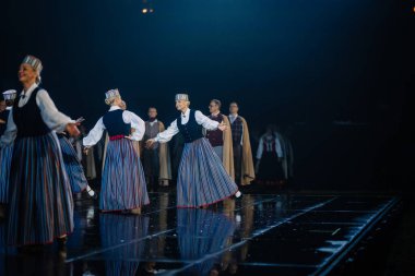 Valmiera, Letonya - 7 Haziran 2025 - GAUJA 80 'deki geleneksel Letonya halk dansları kolajı, renkli kostümlü dansçıları gece aydınlatmalı bir sahnede sergiliyorlar..