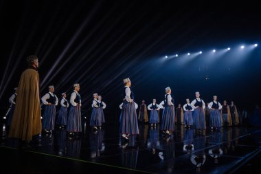 Valmiera, Letonya - 7 Haziran 2025 - GAUJA 80 'deki geleneksel Letonya halk dansları kolajı, renkli kostümlü dansçıları gece aydınlatmalı bir sahnede sergiliyorlar..