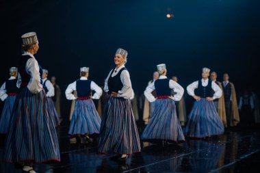 Valmiera, Letonya - 7 Haziran 2025 - GAUJA 80 'deki geleneksel Letonya halk dansları kolajı, renkli kostümlü dansçıları gece aydınlatmalı bir sahnede sergiliyorlar..