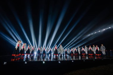 Valmiera, Letonya - 7 Haziran 2025 - GAUJA 80 'deki geleneksel Letonya halk dansları kolajı, renkli kostümlü dansçıları gece aydınlatmalı bir sahnede sergiliyorlar..