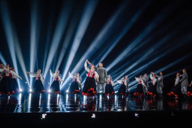 Valmiera, Letonya - 7 Haziran 2025 - GAUJA 80 'deki geleneksel Letonya halk dansları kolajı, renkli kostümlü dansçıları gece aydınlatmalı bir sahnede sergiliyorlar..