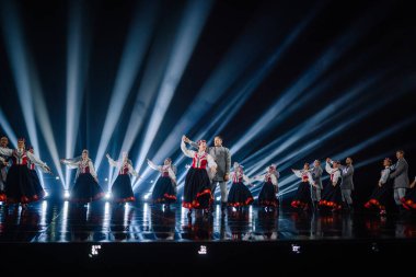 Valmiera, Letonya - 7 Haziran 2025 - GAUJA 80 'deki geleneksel Letonya halk dansları kolajı, renkli kostümlü dansçıları gece aydınlatmalı bir sahnede sergiliyorlar..