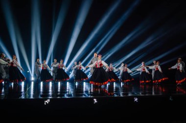 Valmiera, Letonya - 7 Haziran 2025 - GAUJA 80 'deki geleneksel Letonya halk dansları kolajı, renkli kostümlü dansçıları gece aydınlatmalı bir sahnede sergiliyorlar..