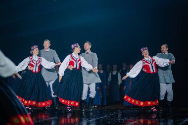 Valmiera, Letonya - 7 Haziran 2025 - GAUJA 80 'deki geleneksel Letonya halk dansları kolajı, renkli kostümlü dansçıları gece aydınlatmalı bir sahnede sergiliyorlar..