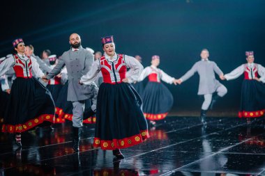 Valmiera, Letonya - 7 Haziran 2025 - GAUJA 80 'deki geleneksel Letonya halk dansları kolajı, renkli kostümlü dansçıları gece aydınlatmalı bir sahnede sergiliyorlar..