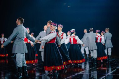 Valmiera, Letonya - 7 Haziran 2025 - GAUJA 80 'deki geleneksel Letonya halk dansları kolajı, renkli kostümlü dansçıları gece aydınlatmalı bir sahnede sergiliyorlar..