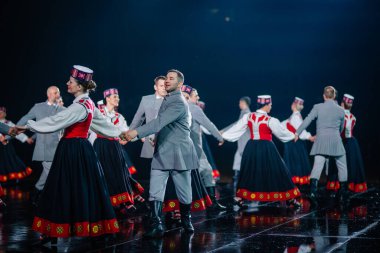 Valmiera, Letonya - 7 Haziran 2025 - GAUJA 80 'deki geleneksel Letonya halk dansları kolajı, renkli kostümlü dansçıları gece aydınlatmalı bir sahnede sergiliyorlar..