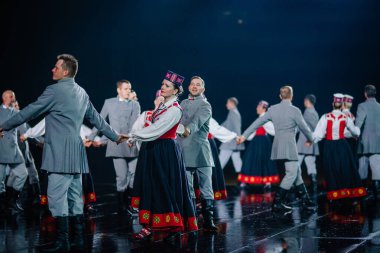 Valmiera, Letonya - 7 Haziran 2025 - GAUJA 80 'deki geleneksel Letonya halk dansları kolajı, renkli kostümlü dansçıları gece aydınlatmalı bir sahnede sergiliyorlar..