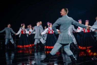 Valmiera, Letonya - 7 Haziran 2025 - GAUJA 80 'deki geleneksel Letonya halk dansları kolajı, renkli kostümlü dansçıları gece aydınlatmalı bir sahnede sergiliyorlar..