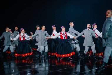 Valmiera, Letonya - 7 Haziran 2025 - GAUJA 80 'deki geleneksel Letonya halk dansları kolajı, renkli kostümlü dansçıları gece aydınlatmalı bir sahnede sergiliyorlar..