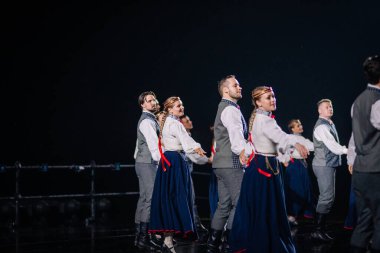 Valmiera, Letonya - 7 Haziran 2025 - GAUJA 80 'deki geleneksel Letonya halk dansları kolajı, renkli kostümlü dansçıları gece aydınlatmalı bir sahnede sergiliyorlar..