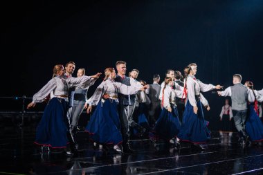 Valmiera, Letonya - 7 Haziran 2025 - GAUJA 80 'deki geleneksel Letonya halk dansları kolajı, renkli kostümlü dansçıları gece aydınlatmalı bir sahnede sergiliyorlar..