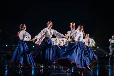 Valmiera, Letonya - 7 Haziran 2025 - GAUJA 80 'deki geleneksel Letonya halk dansları kolajı, renkli kostümlü dansçıları gece aydınlatmalı bir sahnede sergiliyorlar..