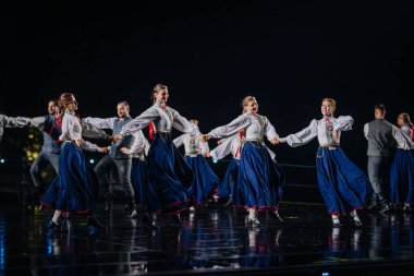 Valmiera, Letonya - 7 Haziran 2025 - GAUJA 80 'deki geleneksel Letonya halk dansları kolajı, renkli kostümlü dansçıları gece aydınlatmalı bir sahnede sergiliyorlar..